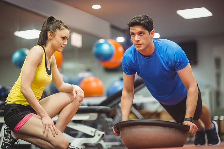 A personal trainer cueing client who is doing stabalization ball pushups