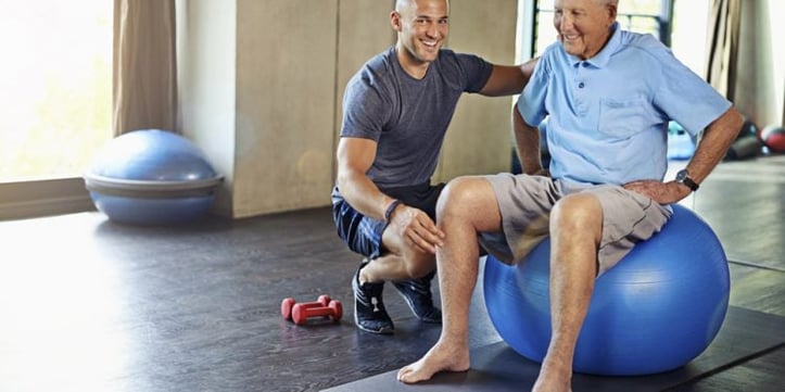 Male trainer assisting elderly man on yoga ball