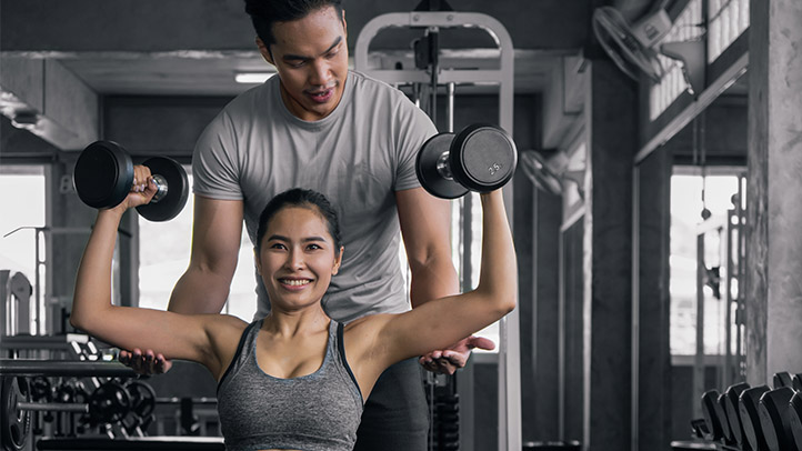 Trainer assisting client with dumbbell shoulder press