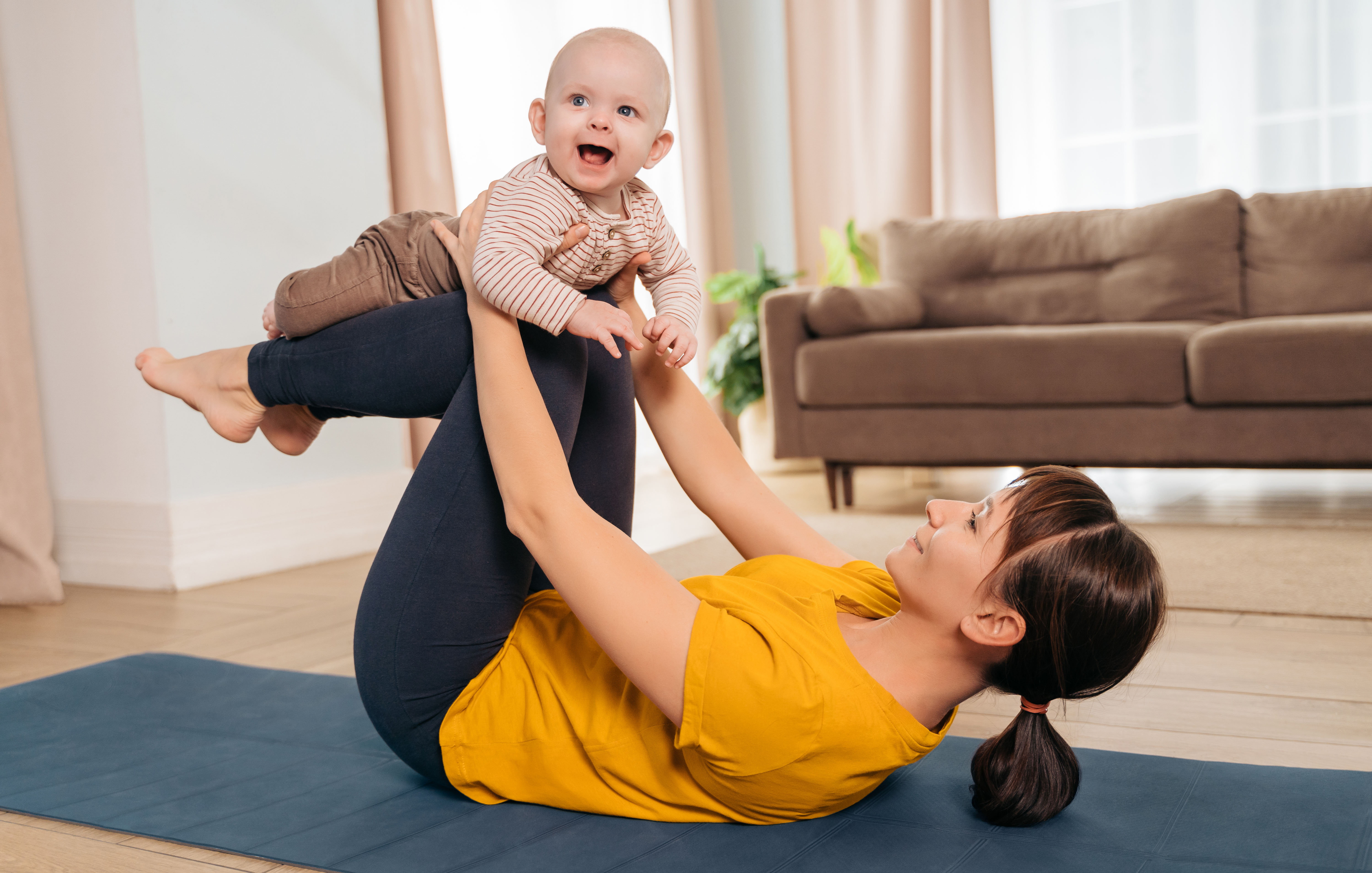 mom laying on a yoga matt with her baby on her legs